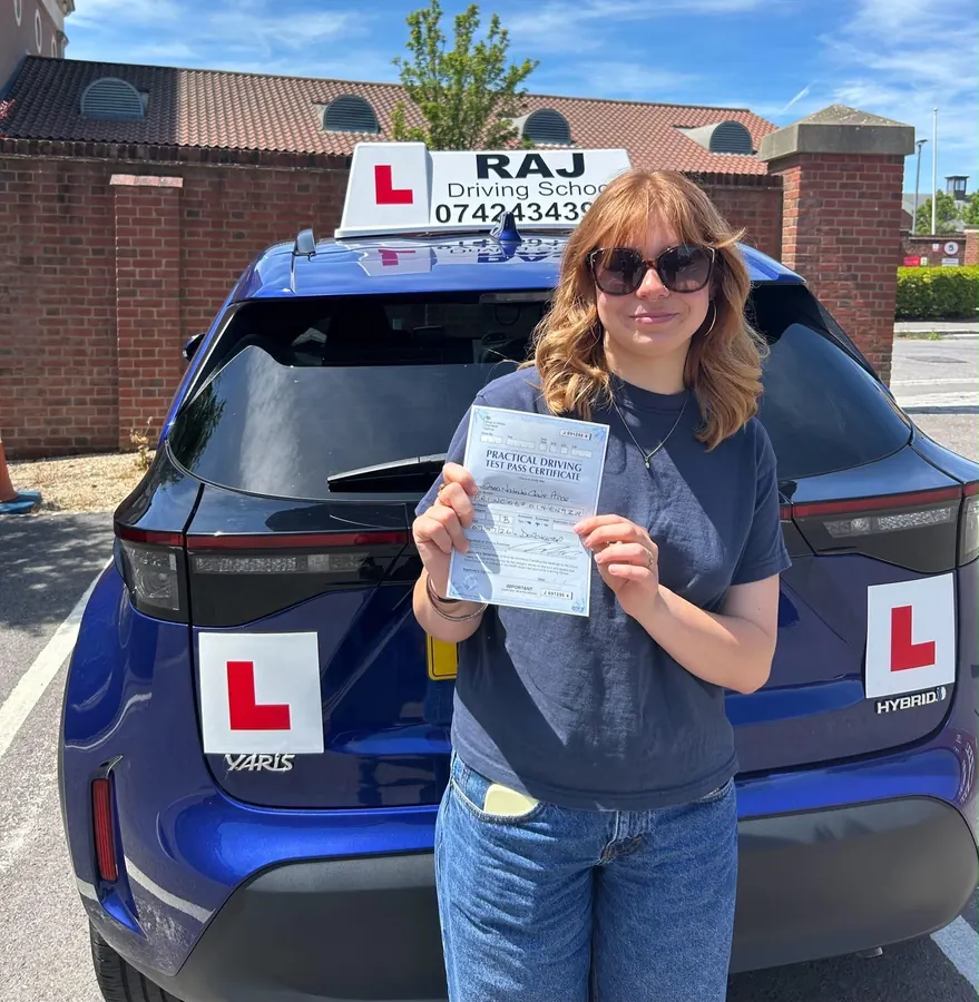 A student holding their driving test pass certificate beside Raj's Toyota Yaris Cross