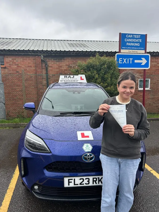 A student holding their driving test pass certificate beside Raj's Toyota Yaris Cross