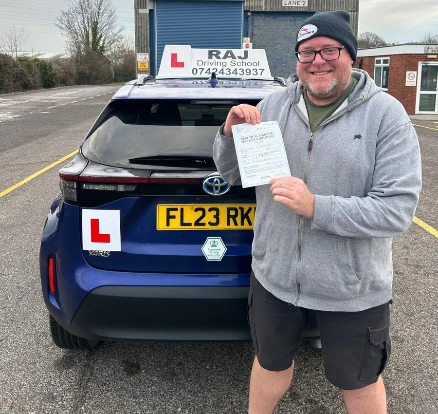 A student holding their driving test pass certificate beside Raj's Toyota Yaris Cross