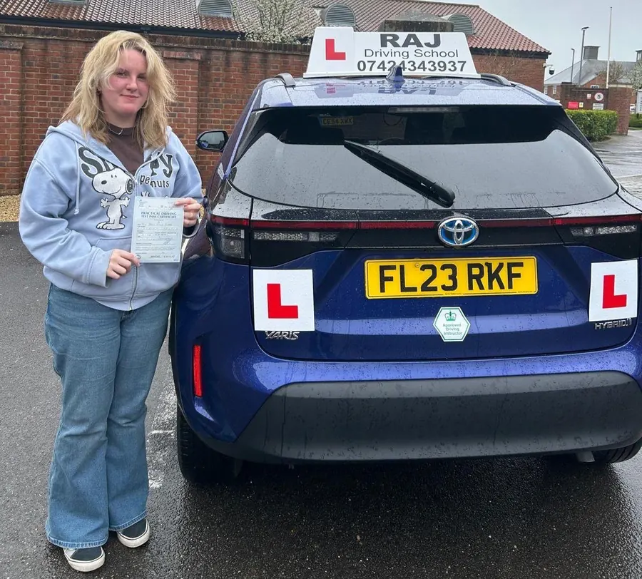 A student holding their driving test pass certificate beside Raj's Toyota Yaris Cross