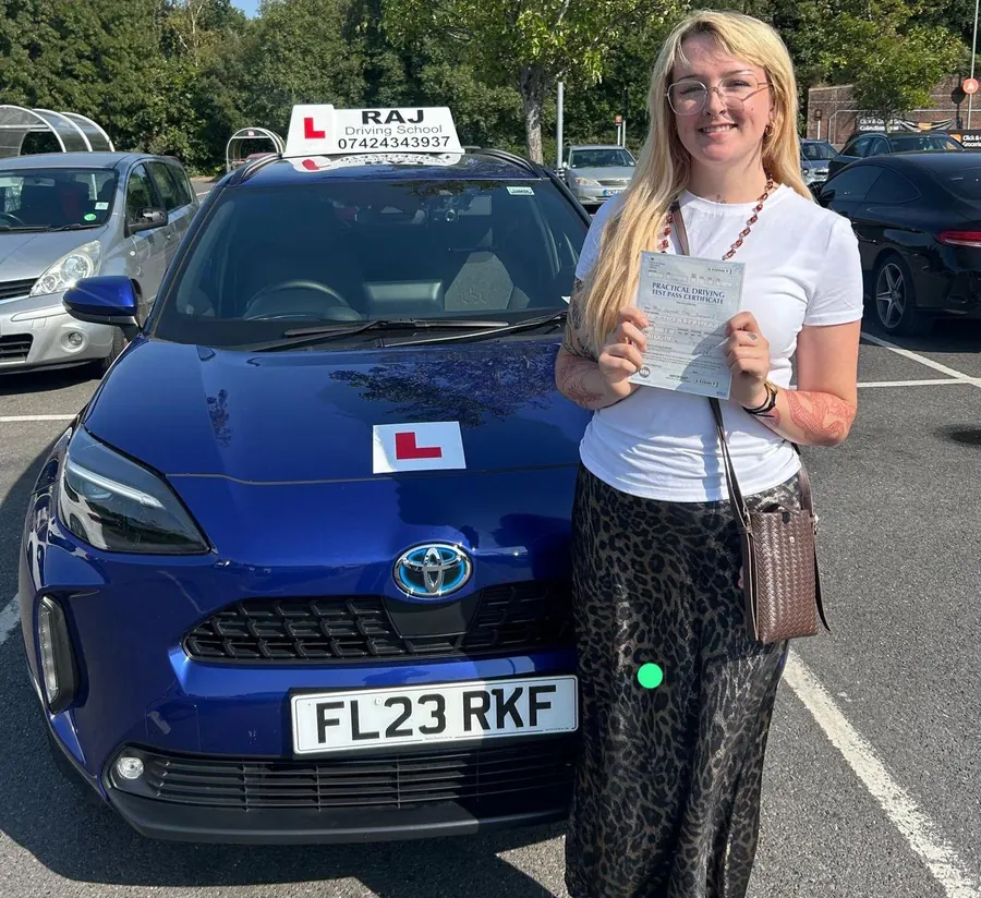 A student holding their driving test pass certificate beside Raj's Toyota Yaris Cross